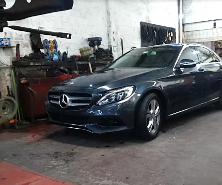 Sedã escuro estacionado dentro da oficina, com bancada de ferramentas ao fundo.